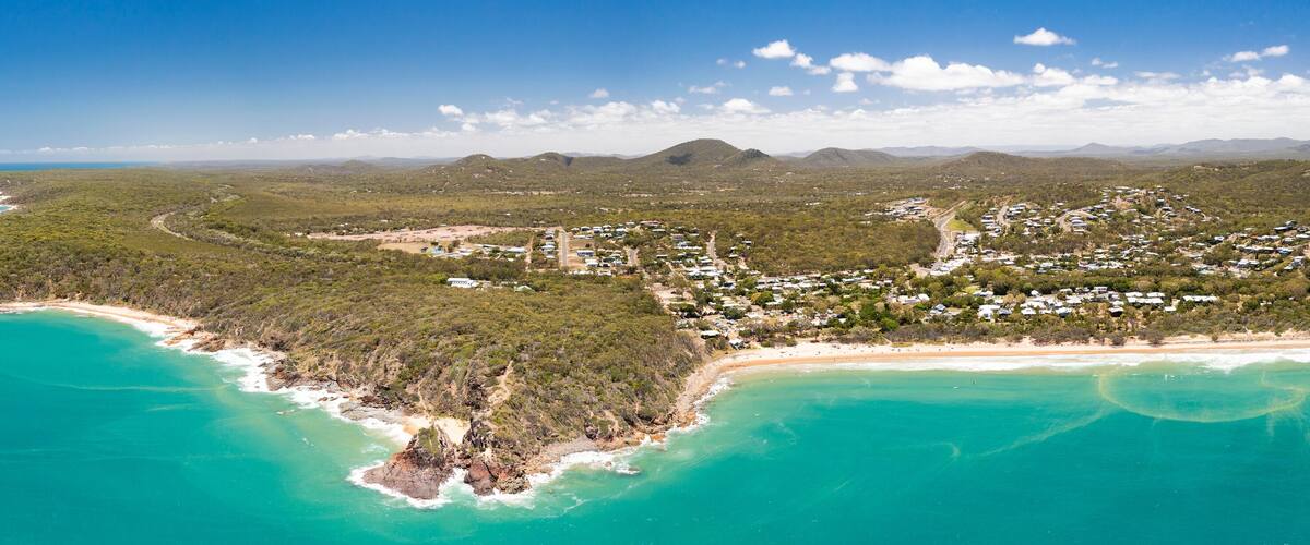 A coastal landscape with a beach, dense forest, and a small settlement.