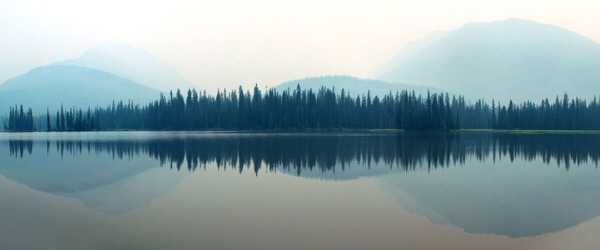 A calm lake with dense forest and mountains in the background.