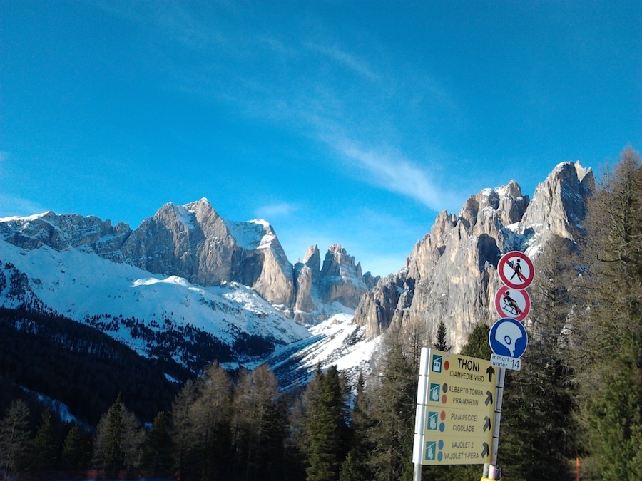 A mountain landscape with snow-covered peaks, a clear blue sky, and a signpost with directional information.