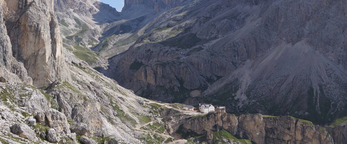A mountain valley with rocky terrain and a small building on a cliff.