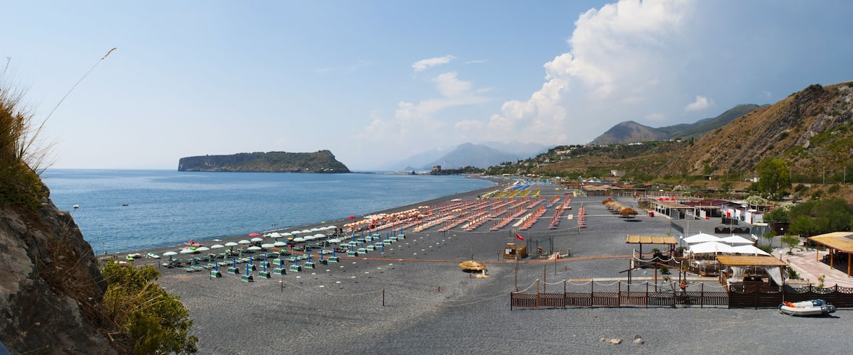 A coastal beach with umbrellas, a boat, and a distant island.