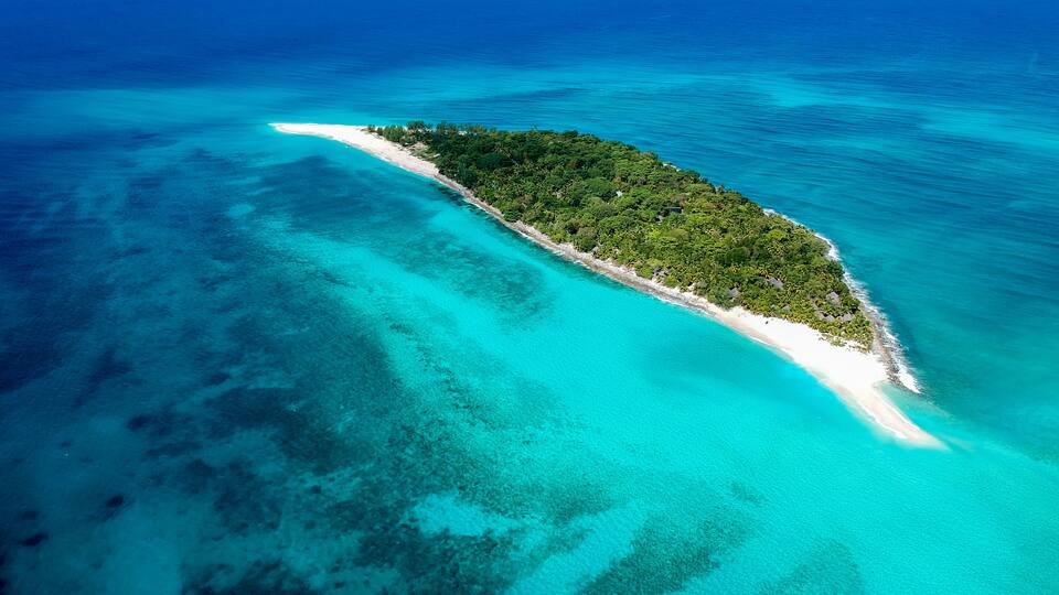 An aerial view of a small island with a white sandy beach and dense green vegetation.