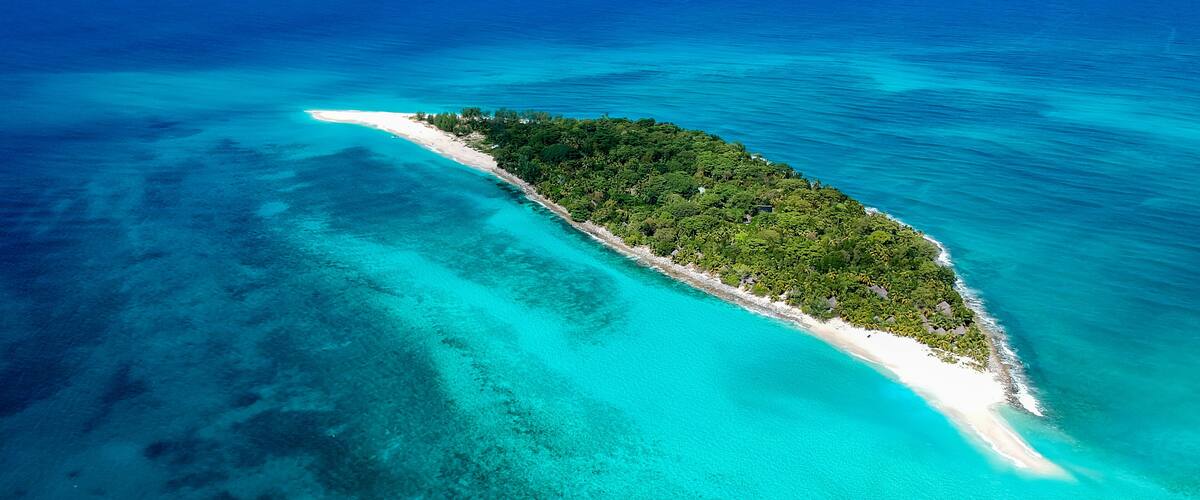 An aerial view of a small island with a white sandy beach and dense green vegetation.