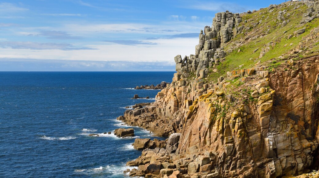 Un paisaje costero con acantilados rocosos, mar azul cristalino y una colina cubierta de hierba.