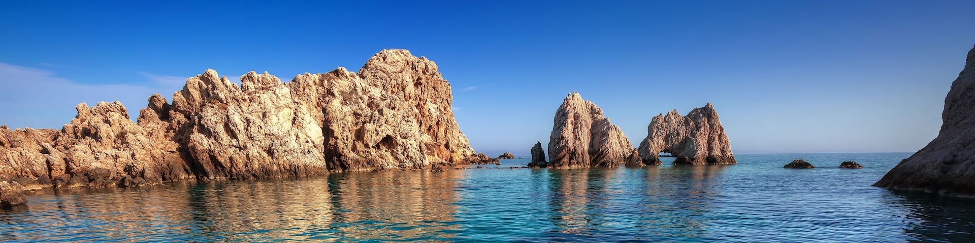 Clear turquoise water, rocky formations, and a clear sky.