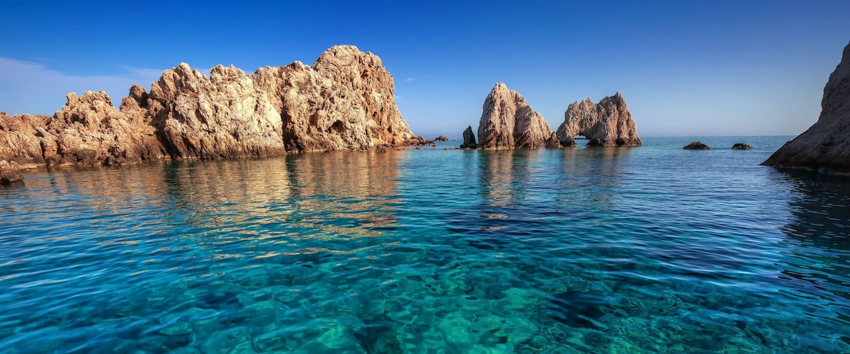 Clear turquoise water, rocky formations, and a clear sky.