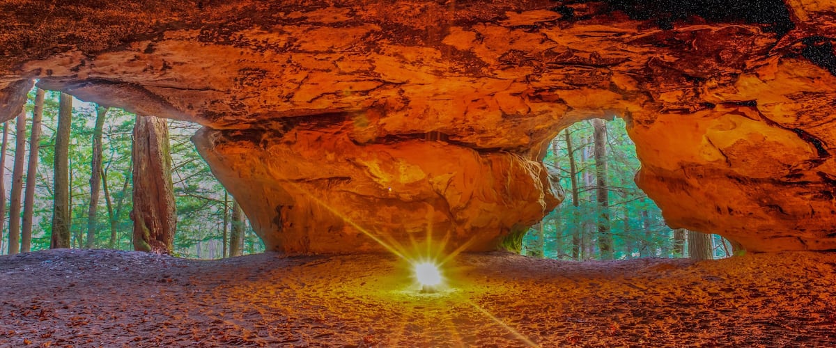 A cave with a glowing light at the bottom and a view of a forest through the cave entrance.