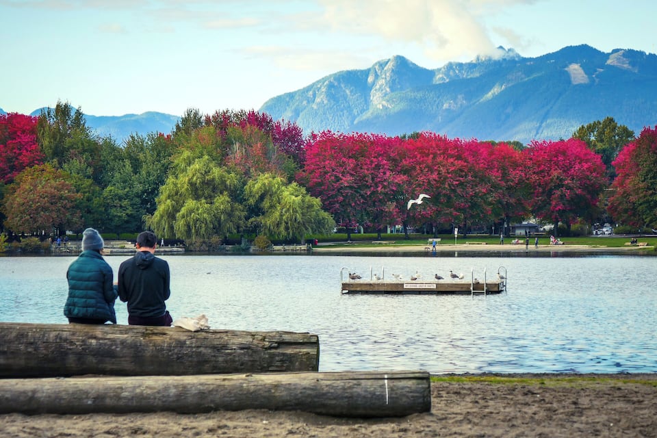 A couple sitting by a lake with mountains in the background.