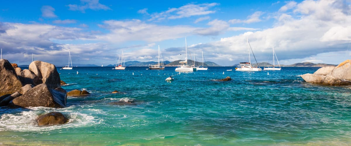 A coastal scene with clear turquoise waters, several sailboats, and rocky formations.