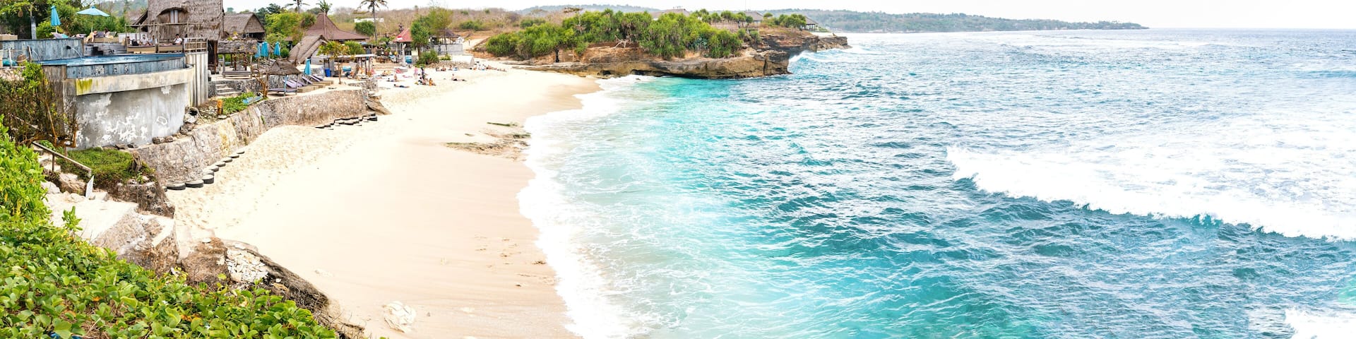 Una playa con aguas turquesas cristalinas, una orilla arenosa y un promontorio rocoso con edificios.