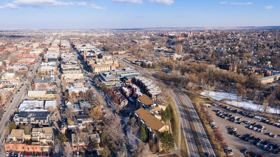 An aerial view of a city with a mix of residential and commercial buildings, a large parking lot, and a river running through the city.