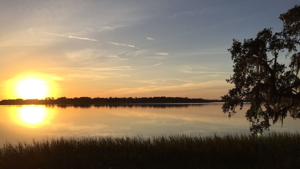 A sunset over a calm lake with a tree on the right and a distant shoreline.