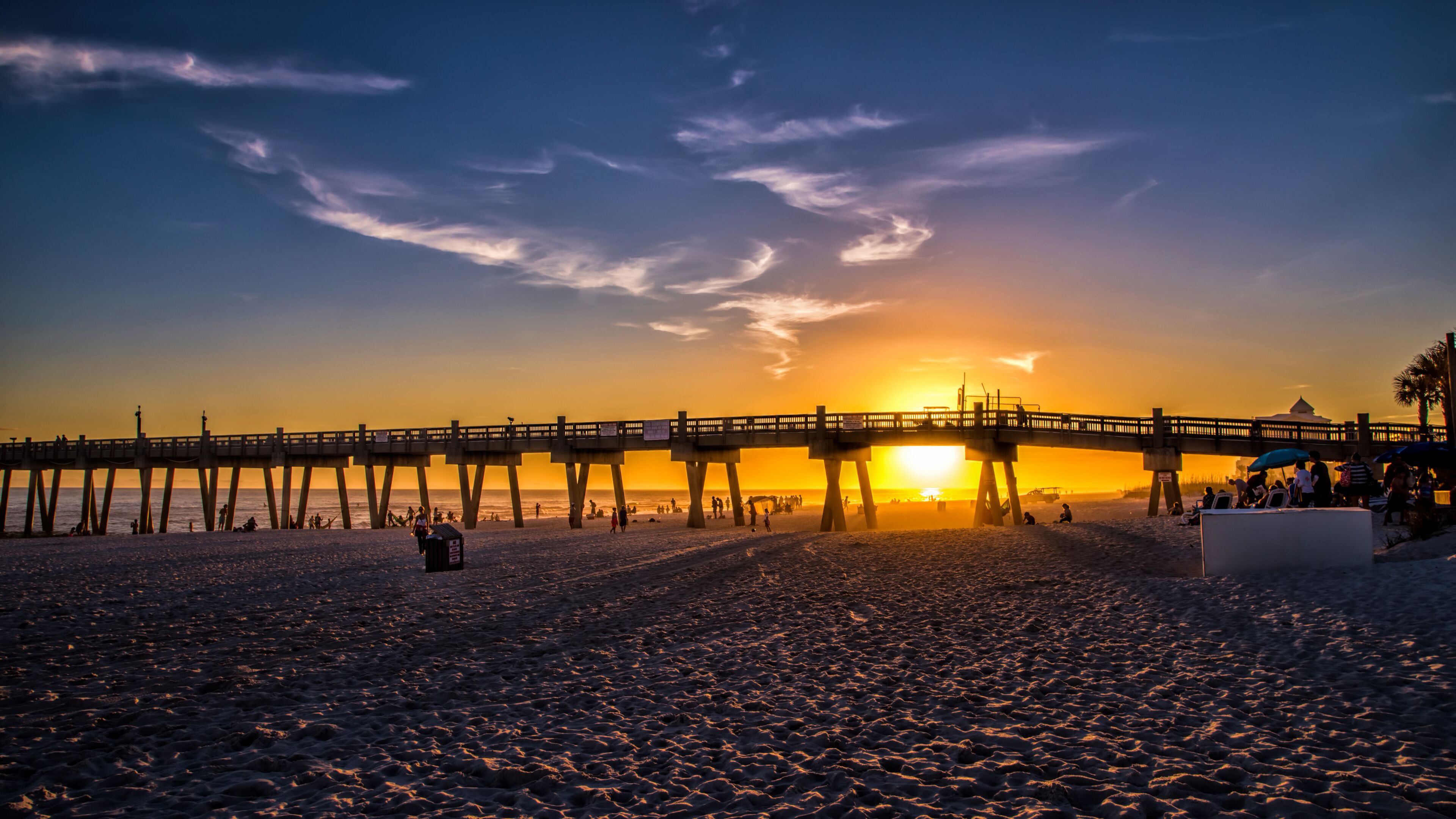 A beach with a pier extending into the water during sunset.