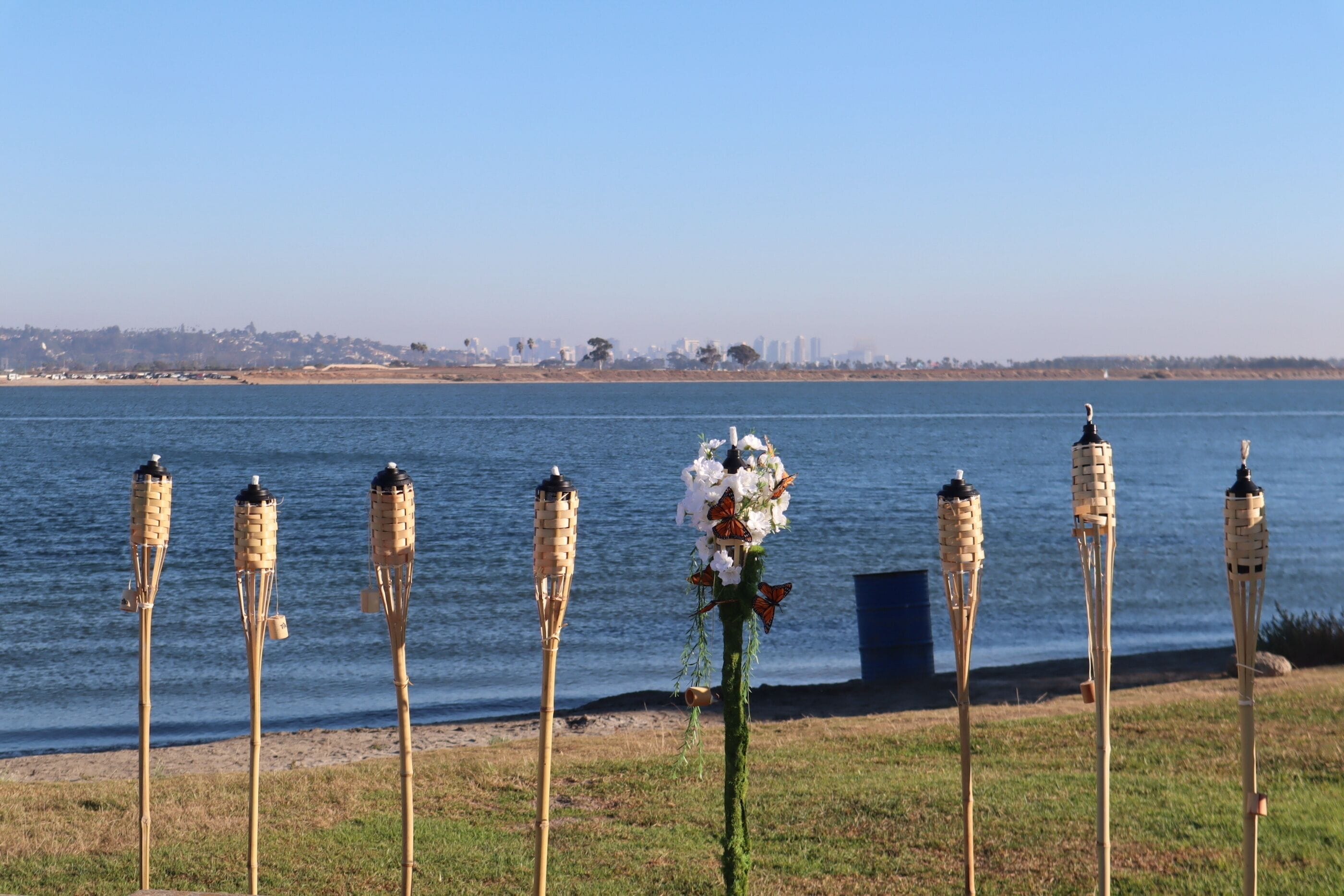 tiki torches with one decorated in flowers standing up in a row in crown point san diego with blue water and sky behind