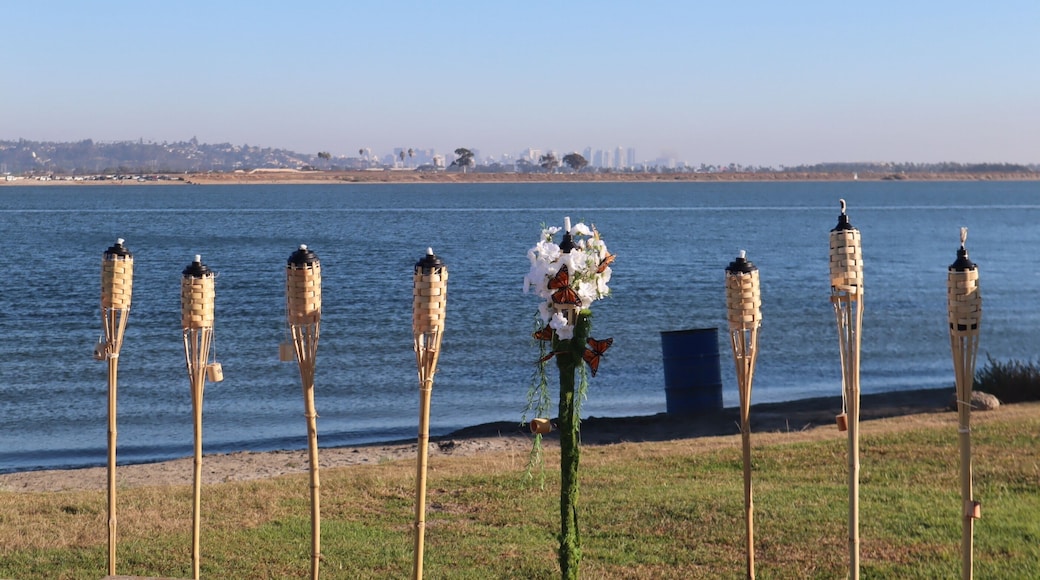 tiki torches with one decorated in flowers standing up in a row in crown point san diego with blue water and sky behind