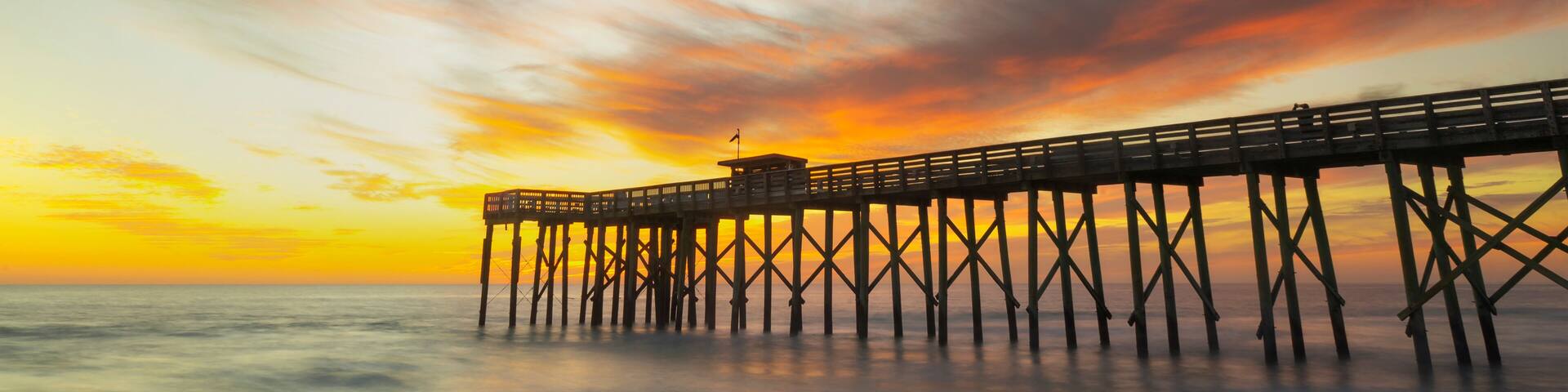 A pier extending into calm waters at sunset with a colorful sky.