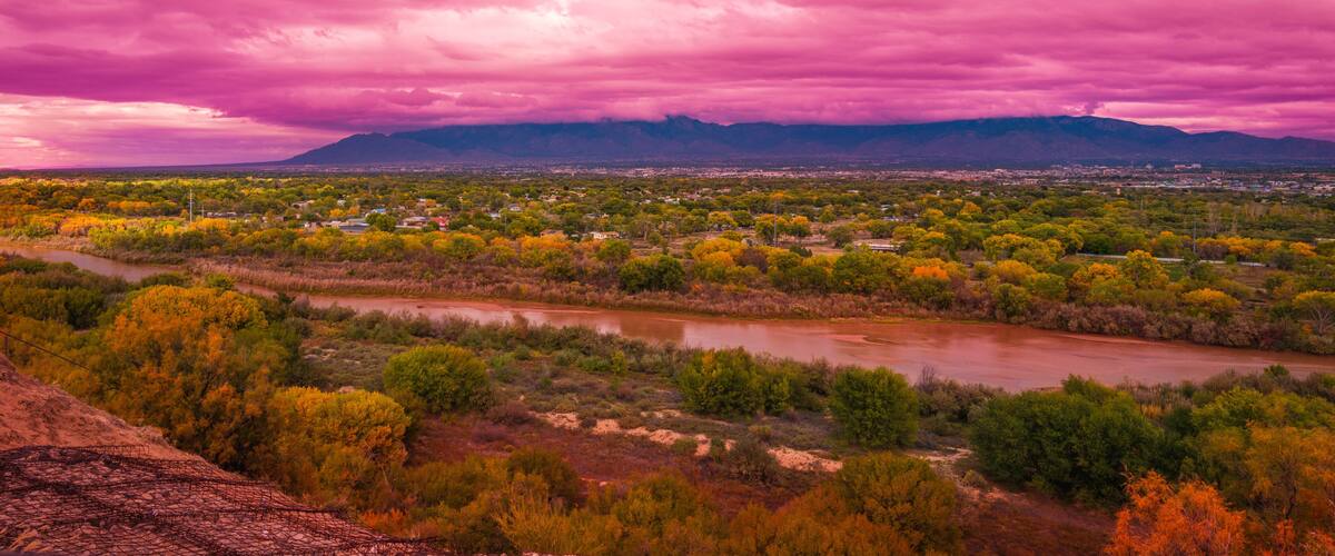 Stormy pink sunset cloudscape over Albuquerque skyline, autumn landscape with colorful cottonwood trees over Rio Grande River, New Mexico, USA