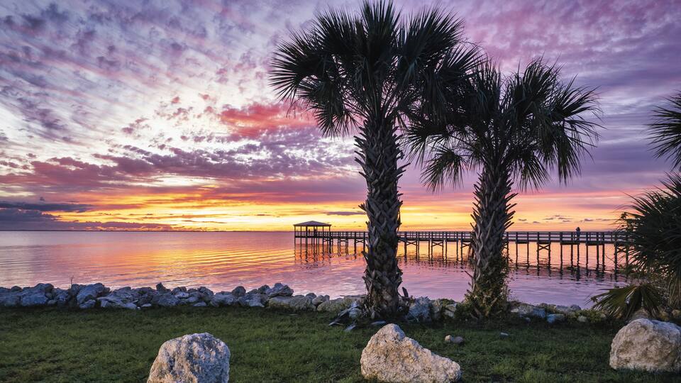 Colorful sunrise over the Rotary Riverfront Park with palms in Titusville, Florida