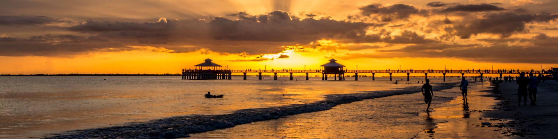 A sunset over a beach with a pier extending into the water, featuring a gazebo structure.