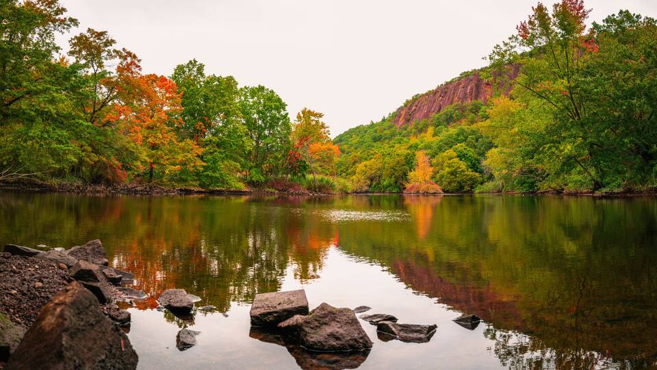 Beautiful fall woodland with rocks and reflections in the river water. Tranquil autumn forest image with space for texts and design. Mill River landscape at East Rock Park in New Haven, Connecticut.