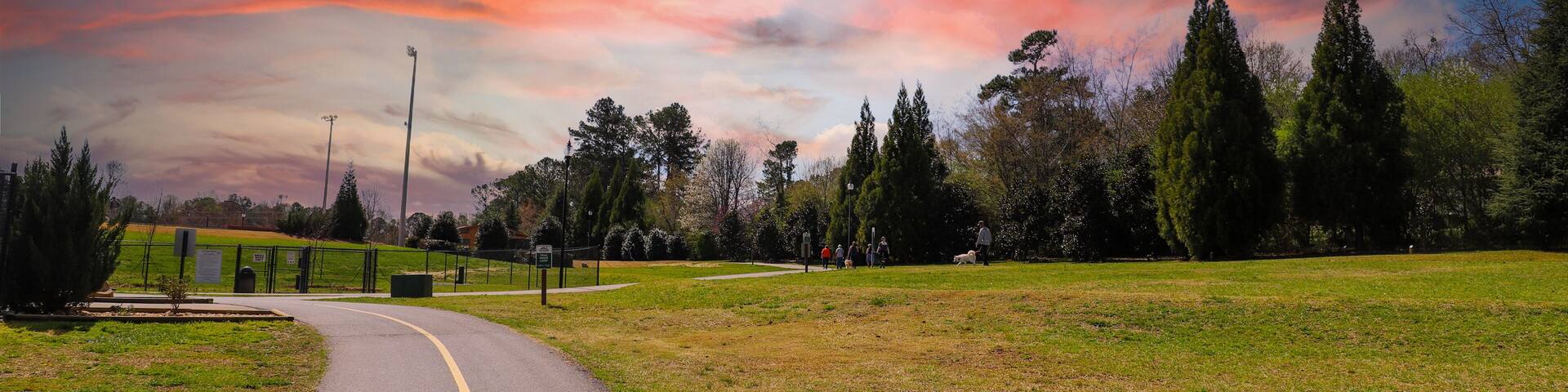 a long winding footpath with a yellow line in the park surrounded by lush green grass and lush green trees with powerful red clouds at sunset at Swift Cantrell Park in Kennesaw Georgia USA