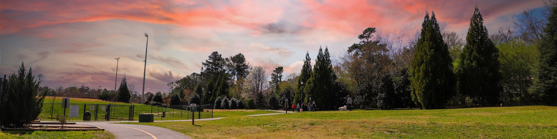 a long winding footpath with a yellow line in the park surrounded by lush green grass and lush green trees with powerful red clouds at sunset at Swift Cantrell Park in Kennesaw Georgia USA