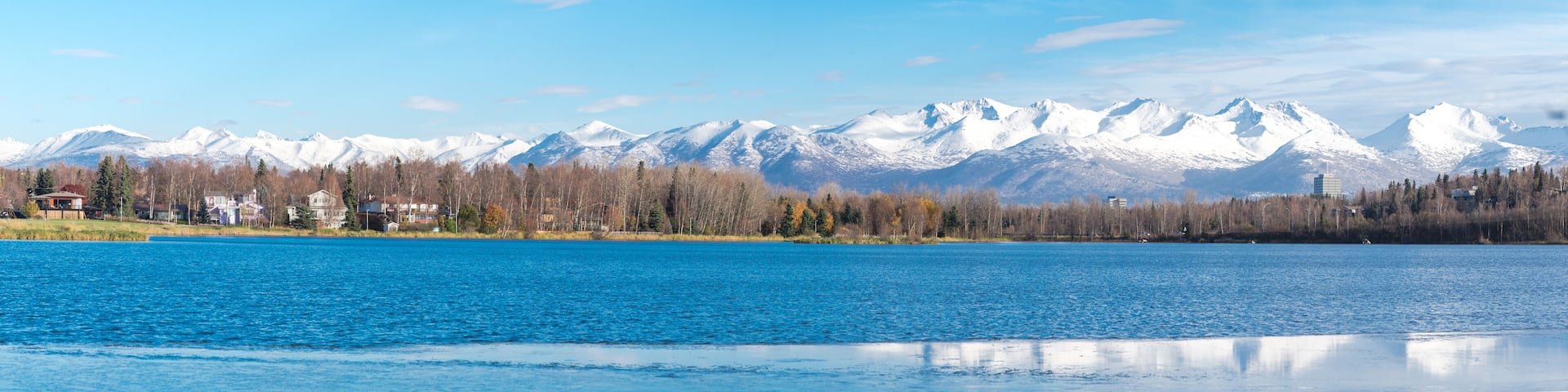 High resolution panorama view row of duplex houses, downtown Anchorage buildings Chugach Mountains in background from Westchester Lagoon