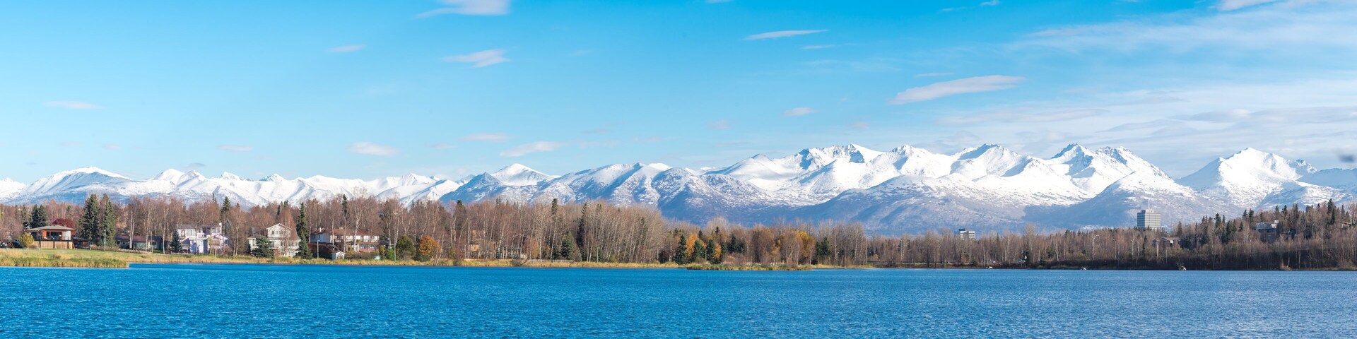 High resolution panorama view row of duplex houses, downtown Anchorage buildings Chugach Mountains in background from Westchester Lagoon