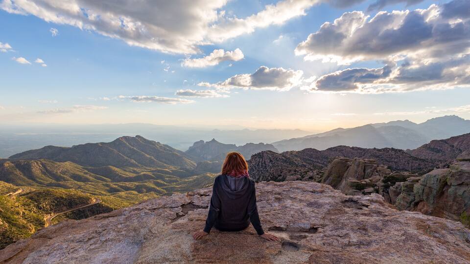 A woman staring down from the top of Mount Lemmon in Arizona while the sun starts to set.