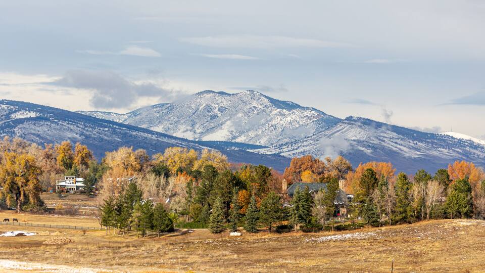 A mountainous landscape with autumn-colored trees and a snow-capped peak in the background.