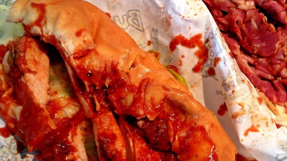 Hot BBQ chicken sandwich with marinara sauce with pastrami sandwich in the back.