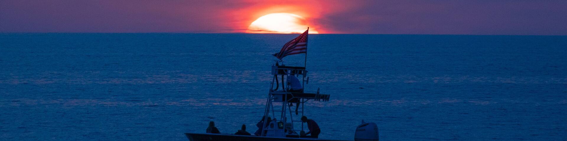 A boat with an American flag on the water during sunset.