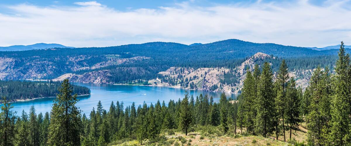 A mountainous landscape with a lake surrounded by dense forests and distant hills.