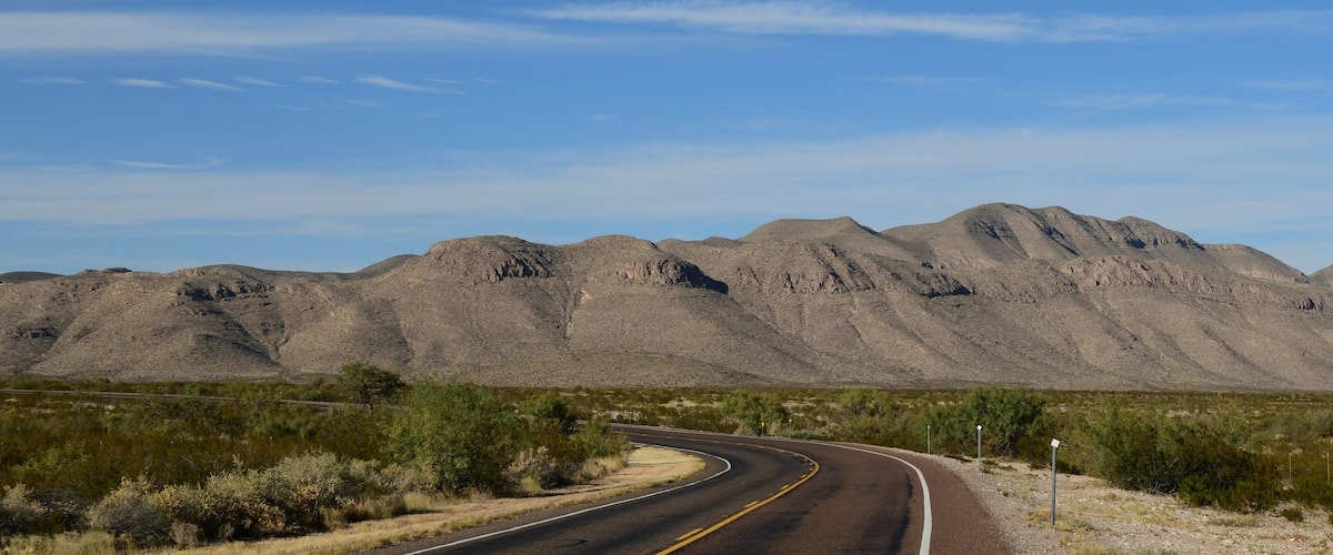 A winding road through a desert landscape with mountains in the background.