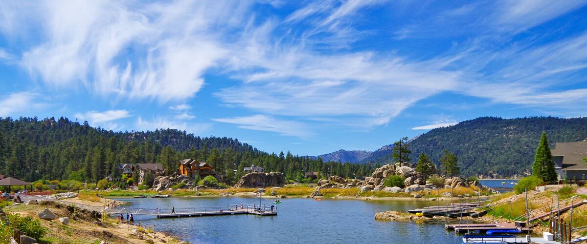 A lake with a dock, surrounded by mountains and houses.