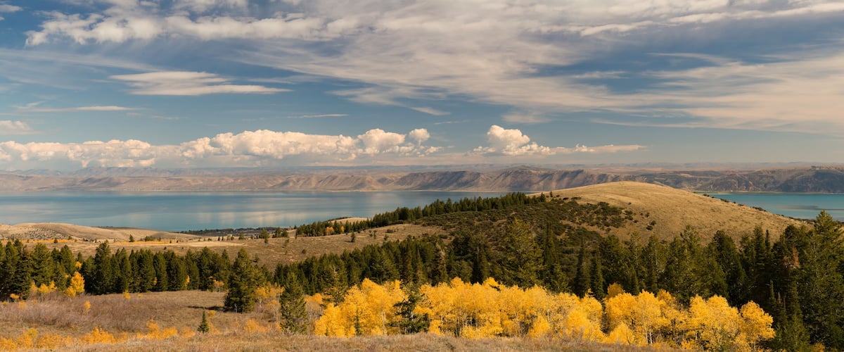 A mountainous landscape with a lake, autumn-colored trees, and a clear sky.