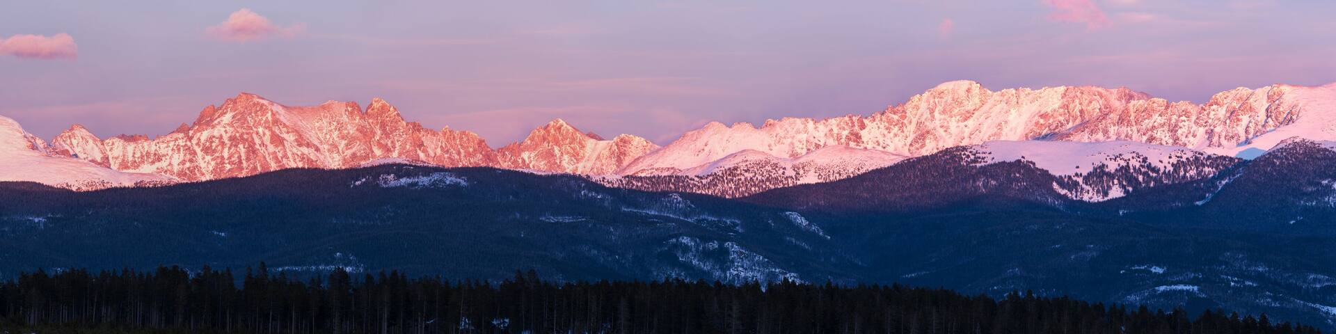 A mountain range with snow-covered peaks and a forested valley.