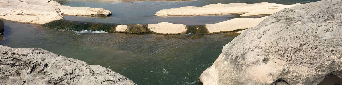 A natural landscape with a river flowing through a rocky terrain, surrounded by hills and sparse vegetation.