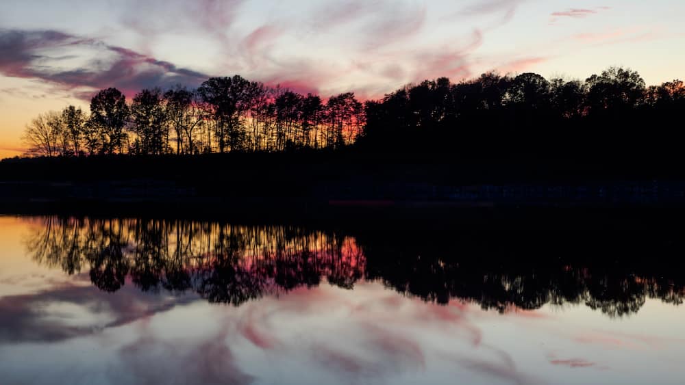 A sunset over a forest reflected in a calm lake.