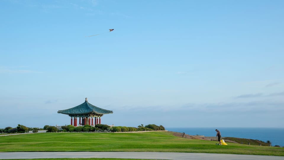 Man Flying a Kite at Angels Gate Park in San Pedro, Ca, under s blue sky with the Korean Frienship Bell in the background