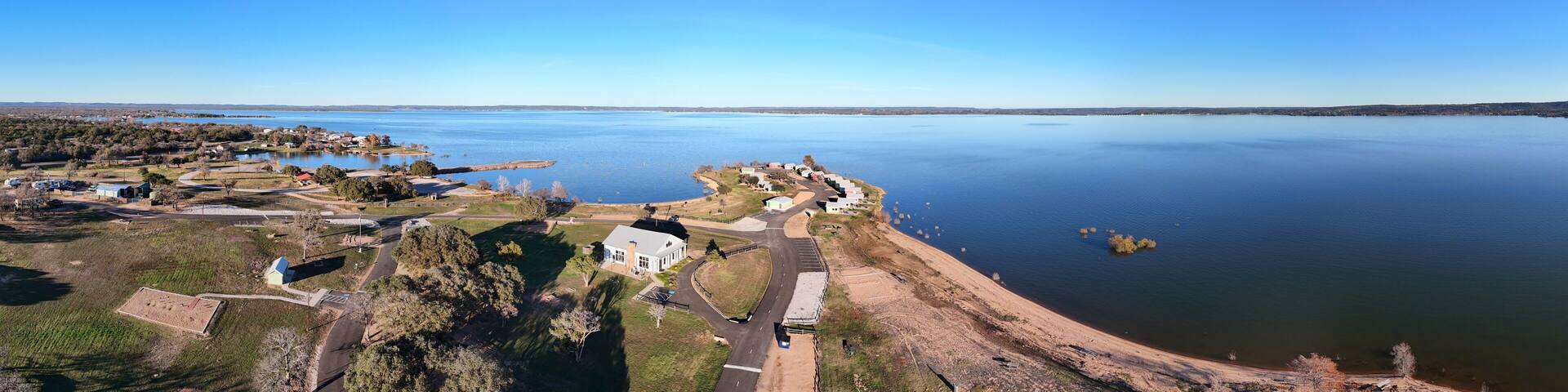 A coastal landscape with a large body of water, a sandy beach, and a cluster of houses near the shore.