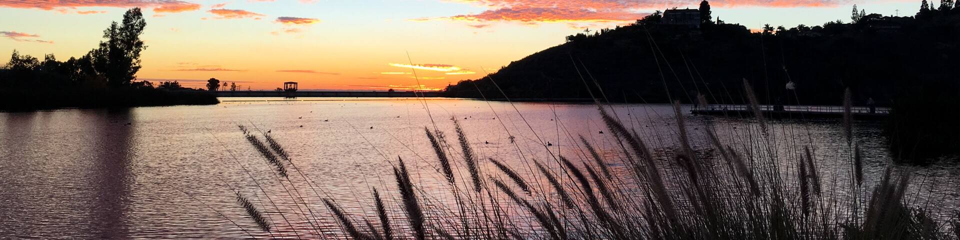 A sunset over a lake with a silhouette of a hill and buildings in the distance.