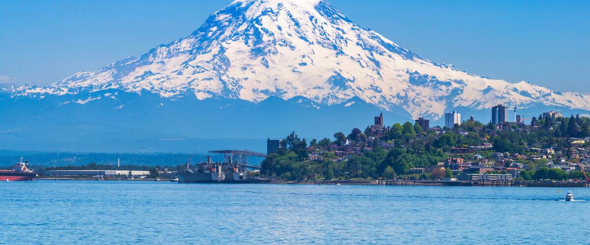 A snow-capped mountain, a body of water, and a cityscape with buildings and greenery.