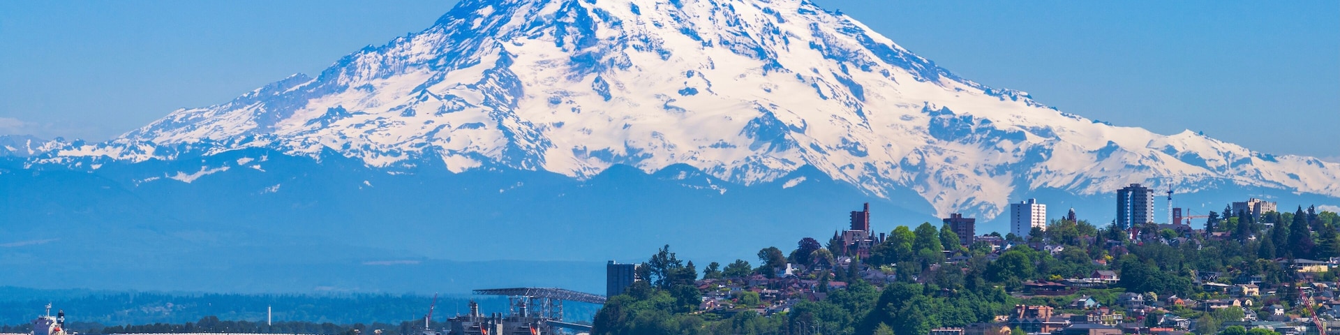 A snow-capped mountain, a body of water, and a cityscape with buildings and greenery.