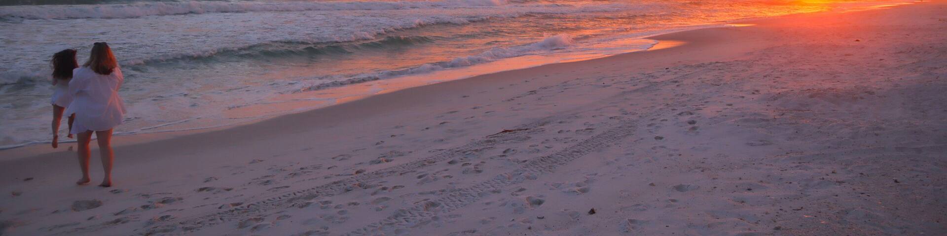 Beautiful peaceful pink orange sunset in Panama City Beach Florida and 2 girls frolicking in the sand