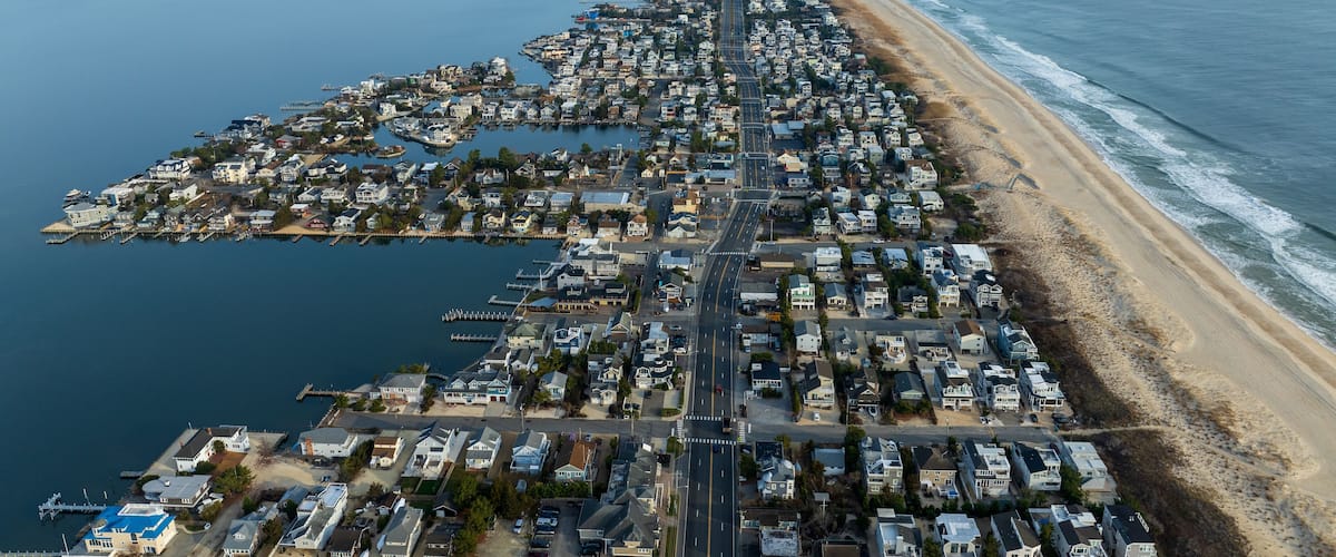 An aerial view of a coastal residential area with a long beachfront, a marina, and a densely packed neighborhood.