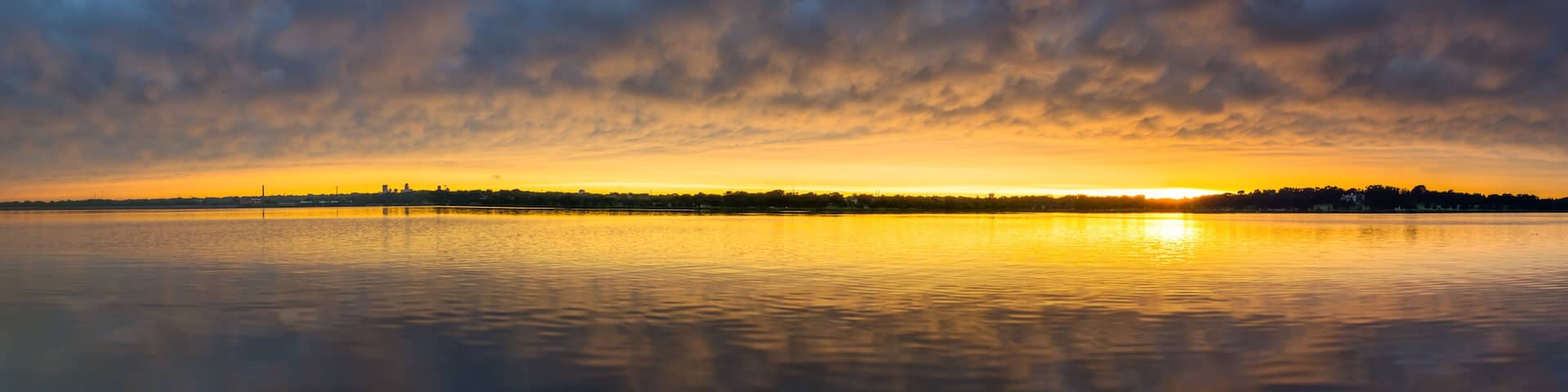 A sunset over a calm body of water with a skyline silhouette in the distance.