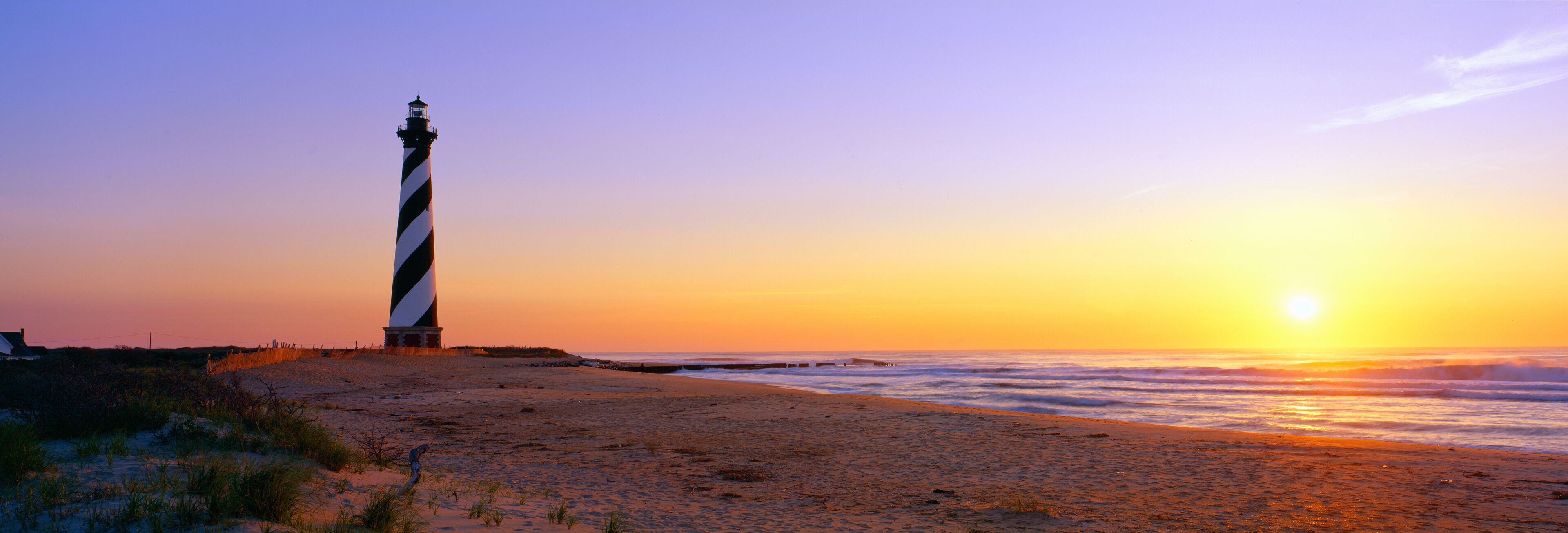 A lighthouse on a beach at sunset.