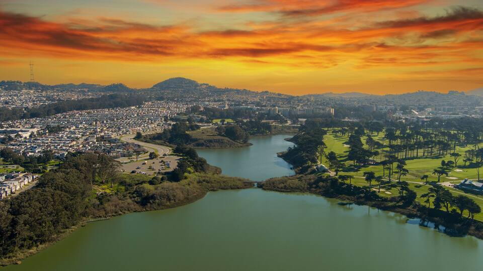 aerial shot of a beautiful spring landscape at Lake Merced with blue lake water and lush green trees, grass and plants at sunset in San Francisco California USA