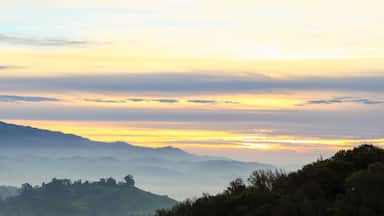 Paisagem montanhosa com nascer ou pôr do sol, com colinas onduladas e atmosfera nebulosa.